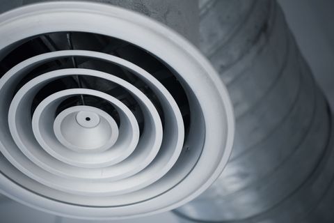 White circular air vent, with concentric rings, attached to a gray duct.