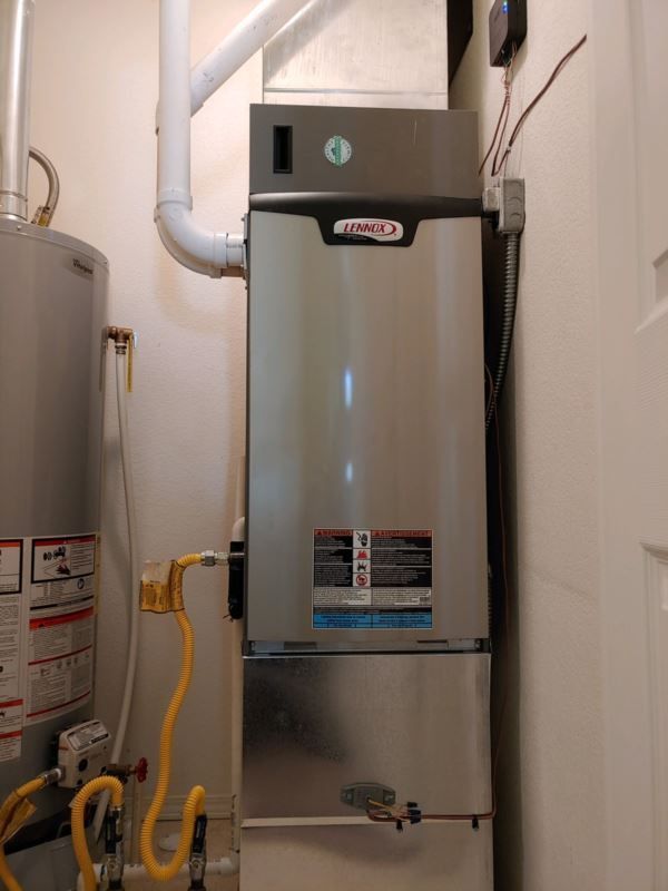 Furnace and hot water heater in a utility closet. Silver and gray furnace. Gray water heater. Yellow gas lines.