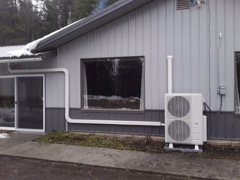 Exterior view of a building with a white HVAC unit, window, and gutter in a snowy setting.