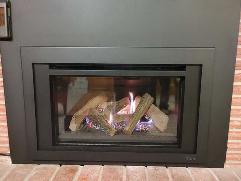 A modern fireplace with a black frame and burning gas logs, set in a brick wall.