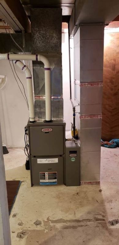 A gray Lennox furnace and water heater in a basement. White pipes are connected to the furnace. Concrete floor.
