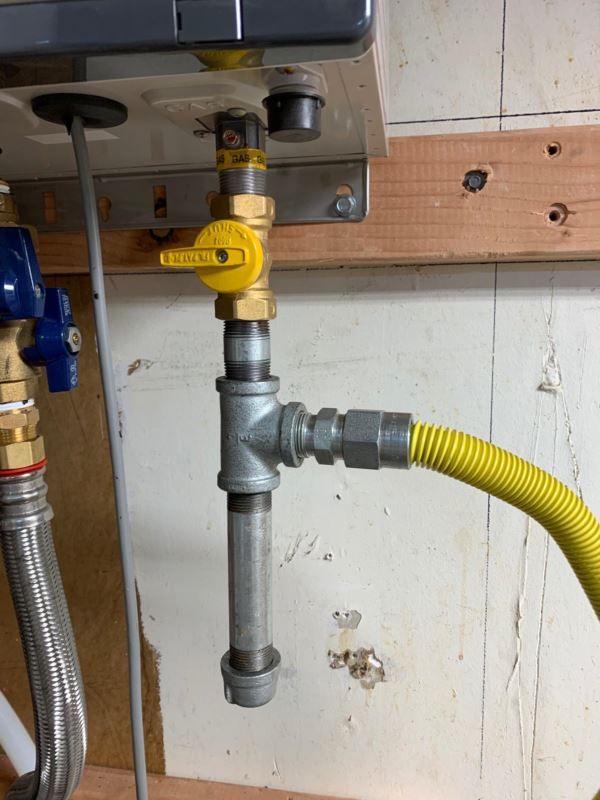 Gas line connection to a water heater, with yellow flex hose and shut-off valve.