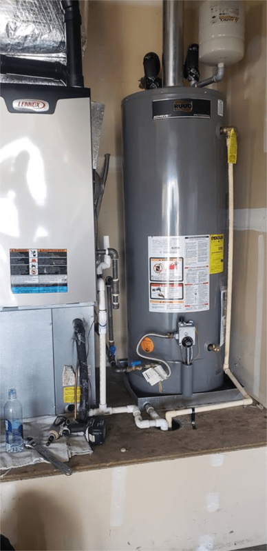 Water heater and furnace against a beige wall, pipes visible, on a wooden platform.
