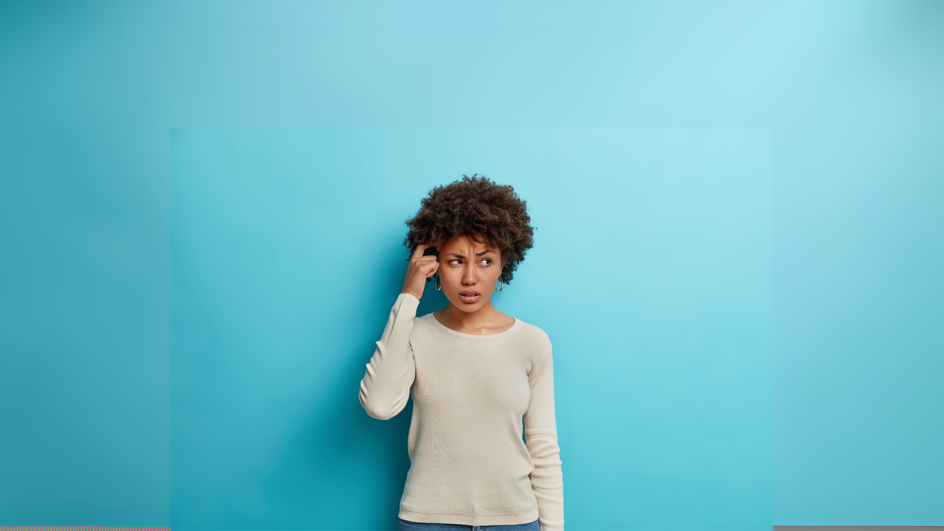 Woman with curly hair, touching her head, looking thoughtful, against a blue backdrop.
