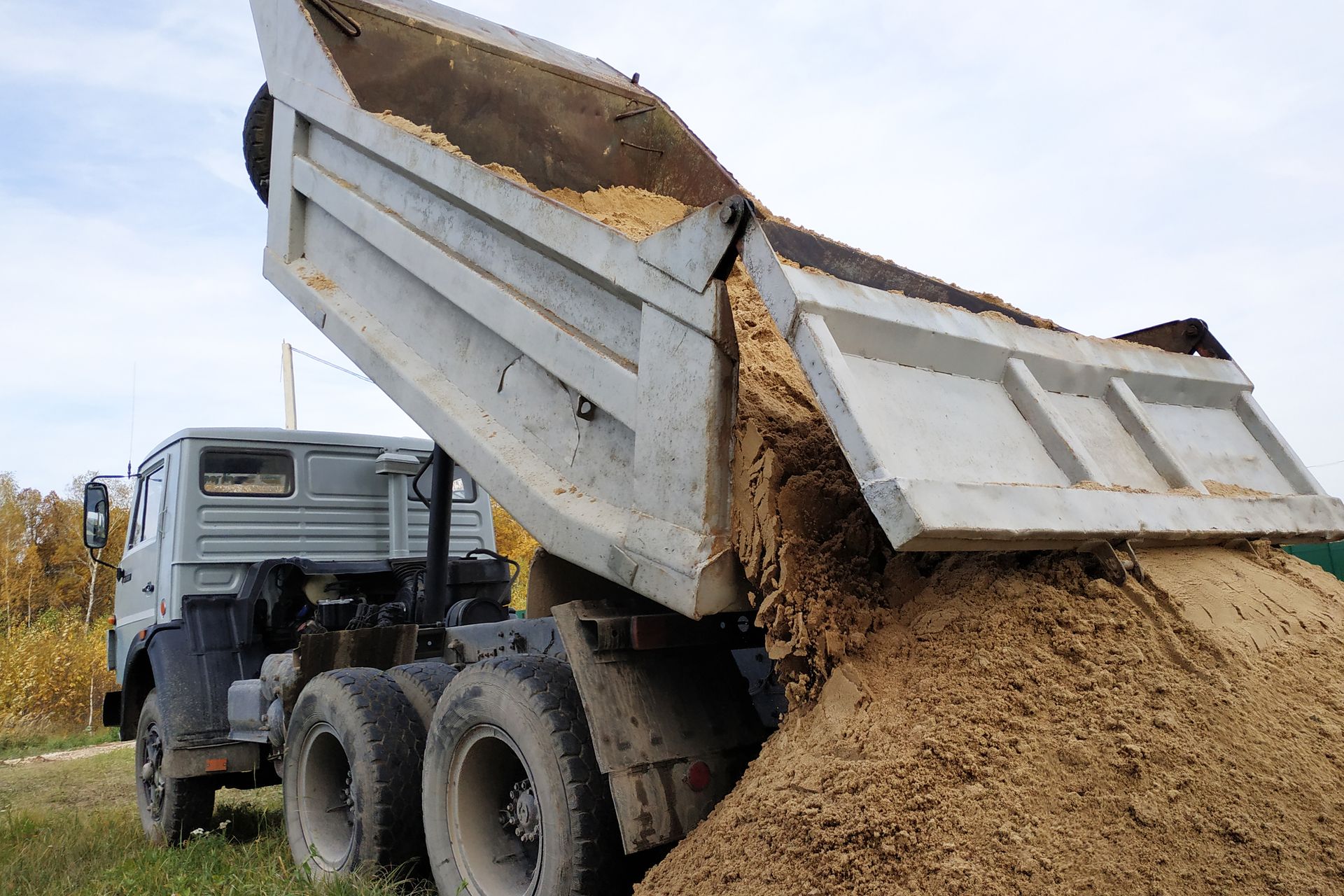 A dump truck is dumping a large pile of dirt.