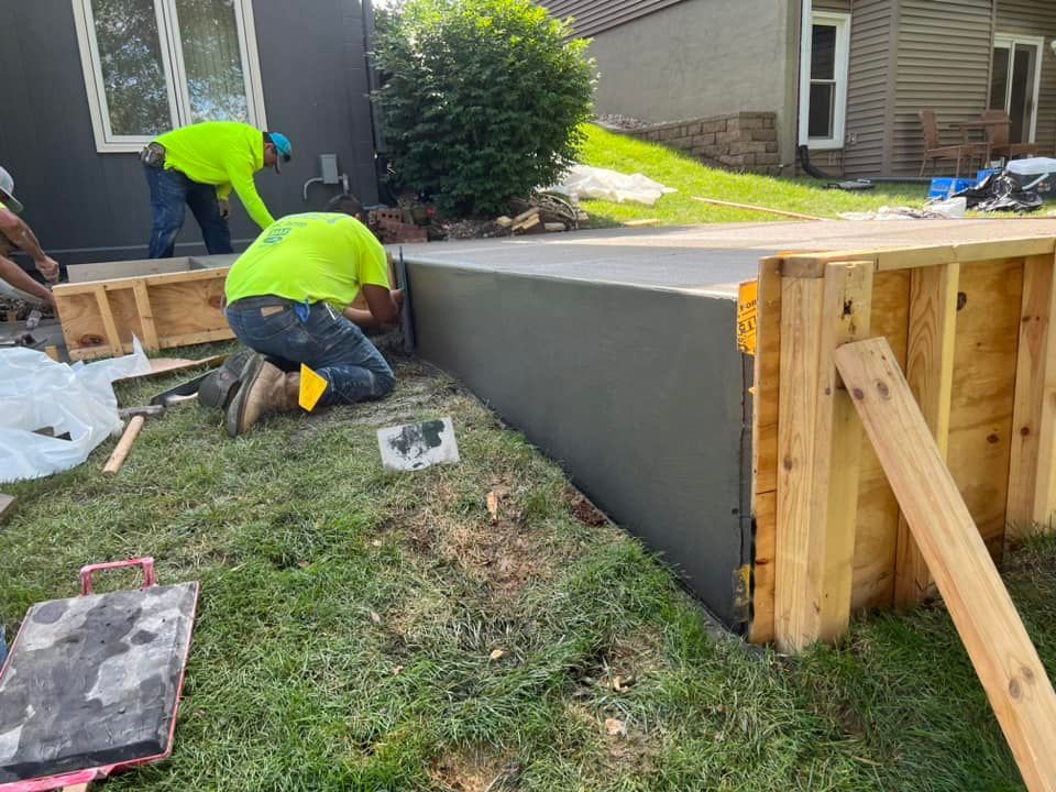 A group of men are working on a concrete wall in front of a house.