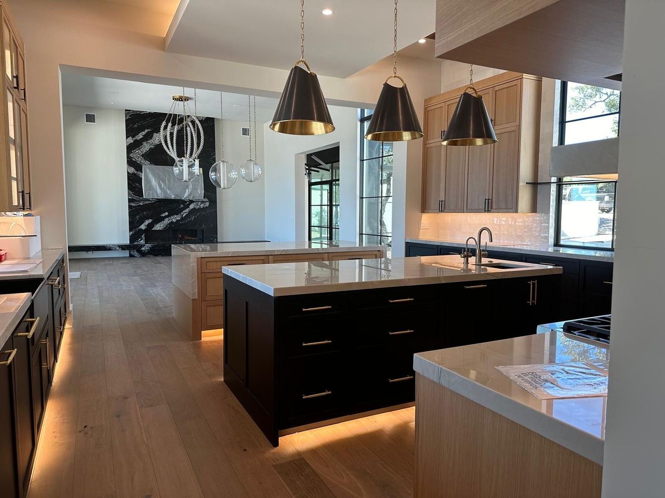 Modern kitchen with black and light cabinets, multiple islands, pendant lights, and a fireplace.