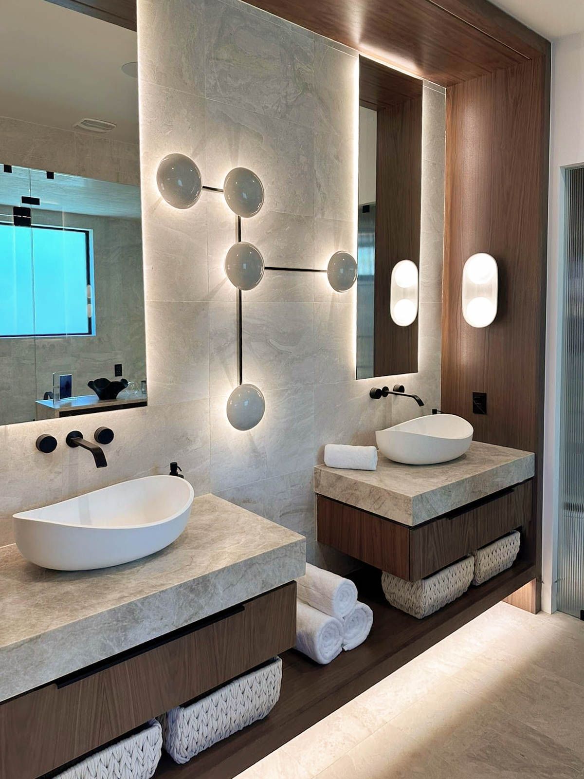 Modern bathroom with two stone-topped vanities, vessel sinks, and unique wall sconces.