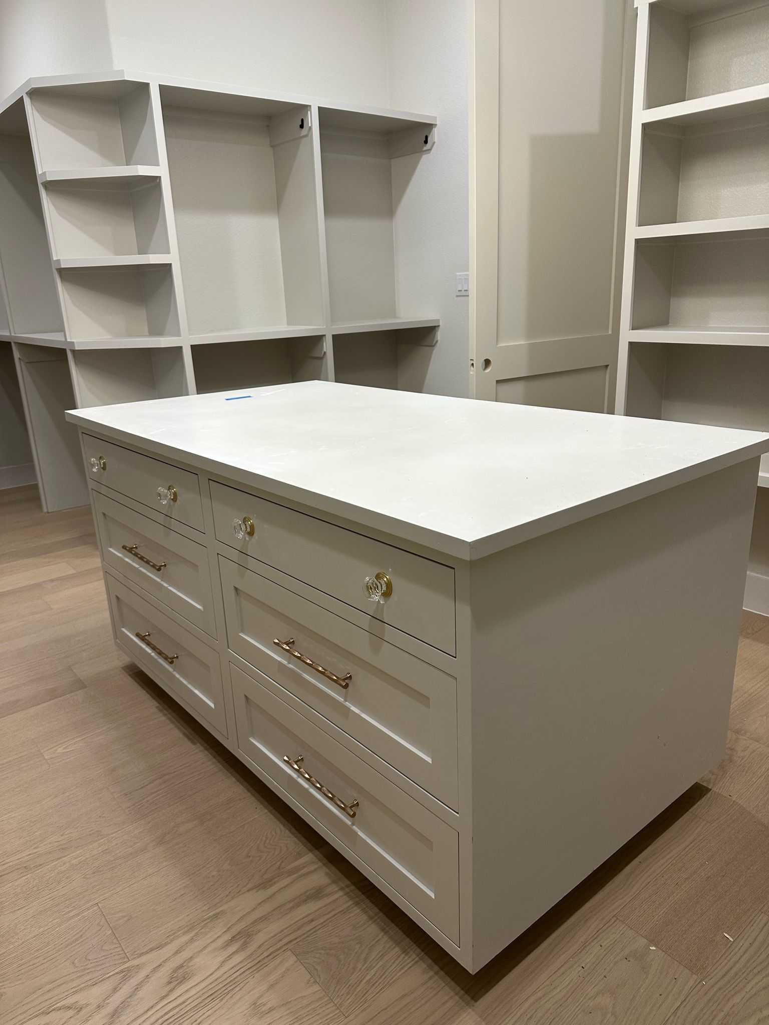 Two tall apartment buildings with lush trees and plants on balconies against a blue sky.