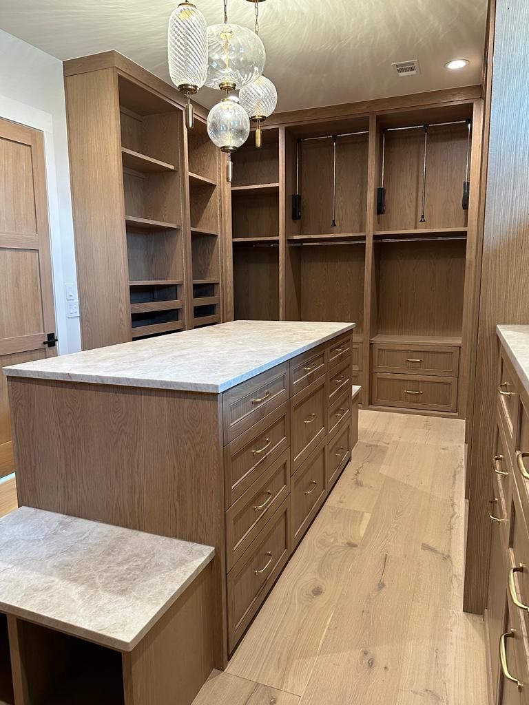 Walk-in closet with wooden shelves, drawers, and an island. Light wood flooring and countertops.