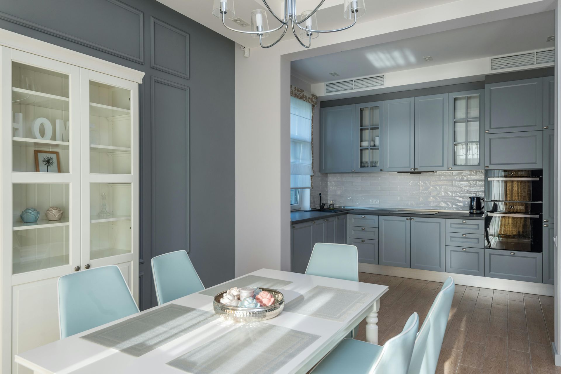 Dining room with a white table and blue chairs, leading to a blue kitchen.