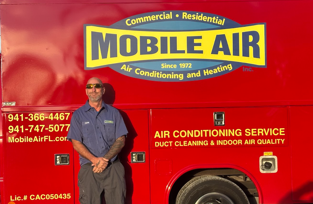 Man in blue shirt stands by a red Mobile Air service truck. Truck has logo and contact info.