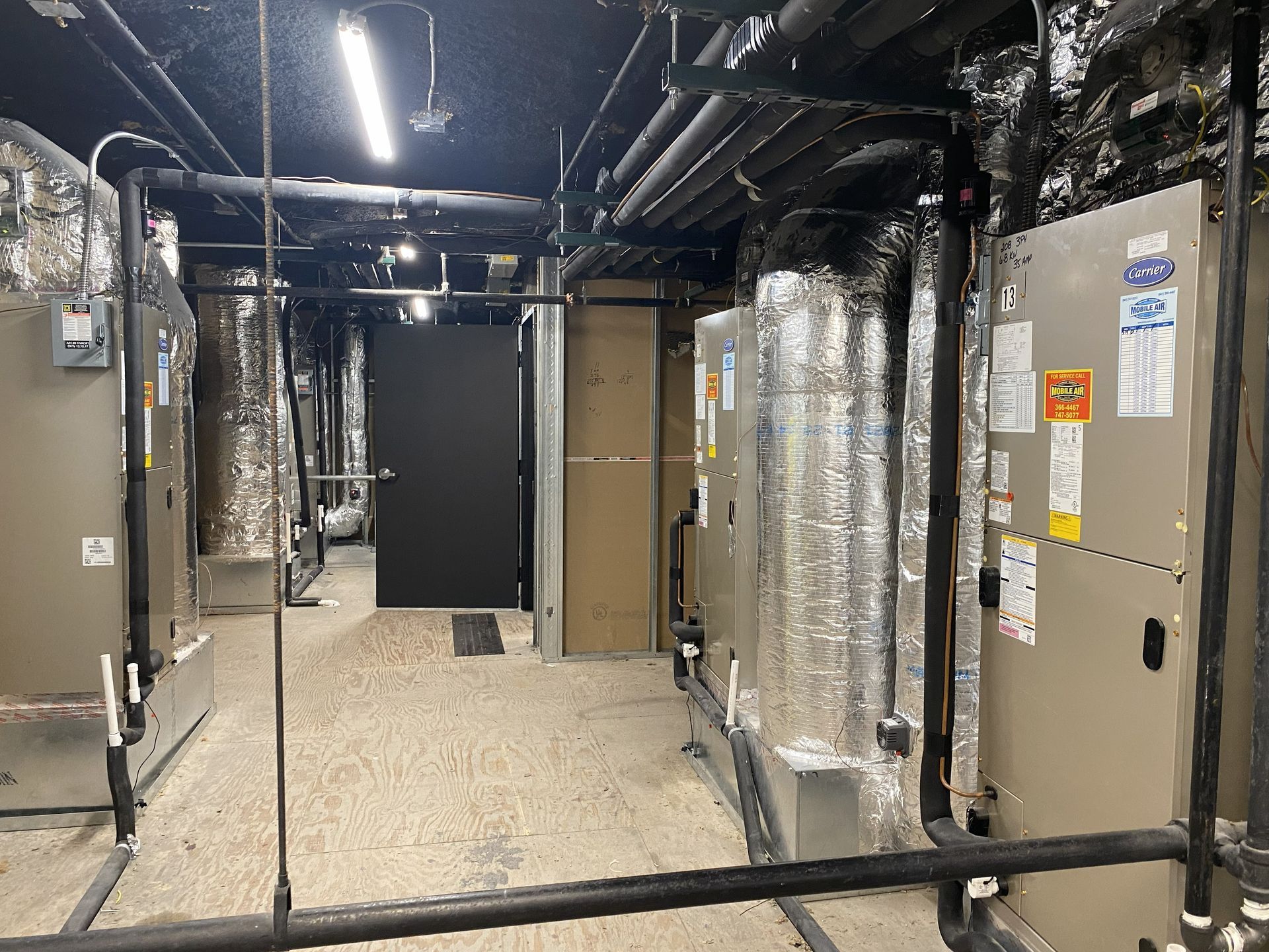 Mechanical room with HVAC units, pipes, and a door.
