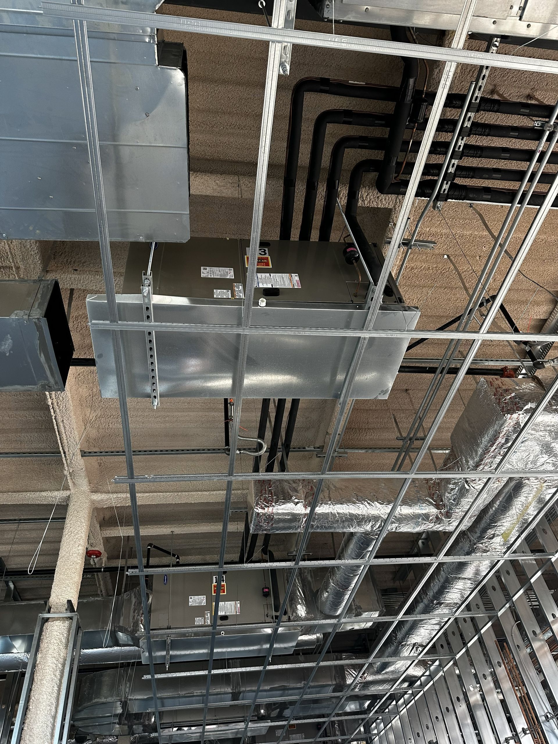 Overhead view of unfinished ceiling with metal framework, ductwork, and black pipes.