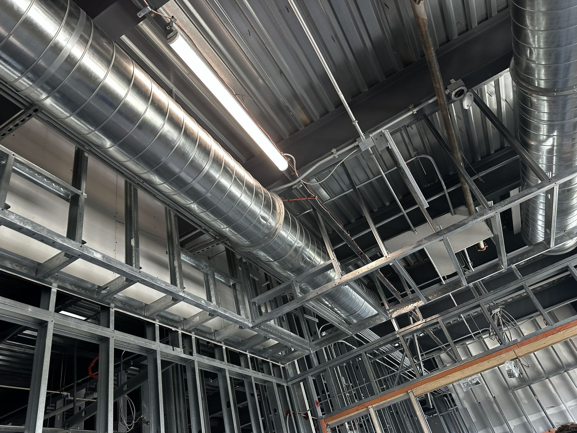 Construction site interior, metal framework, ductwork, and exposed ceiling fixtures.
