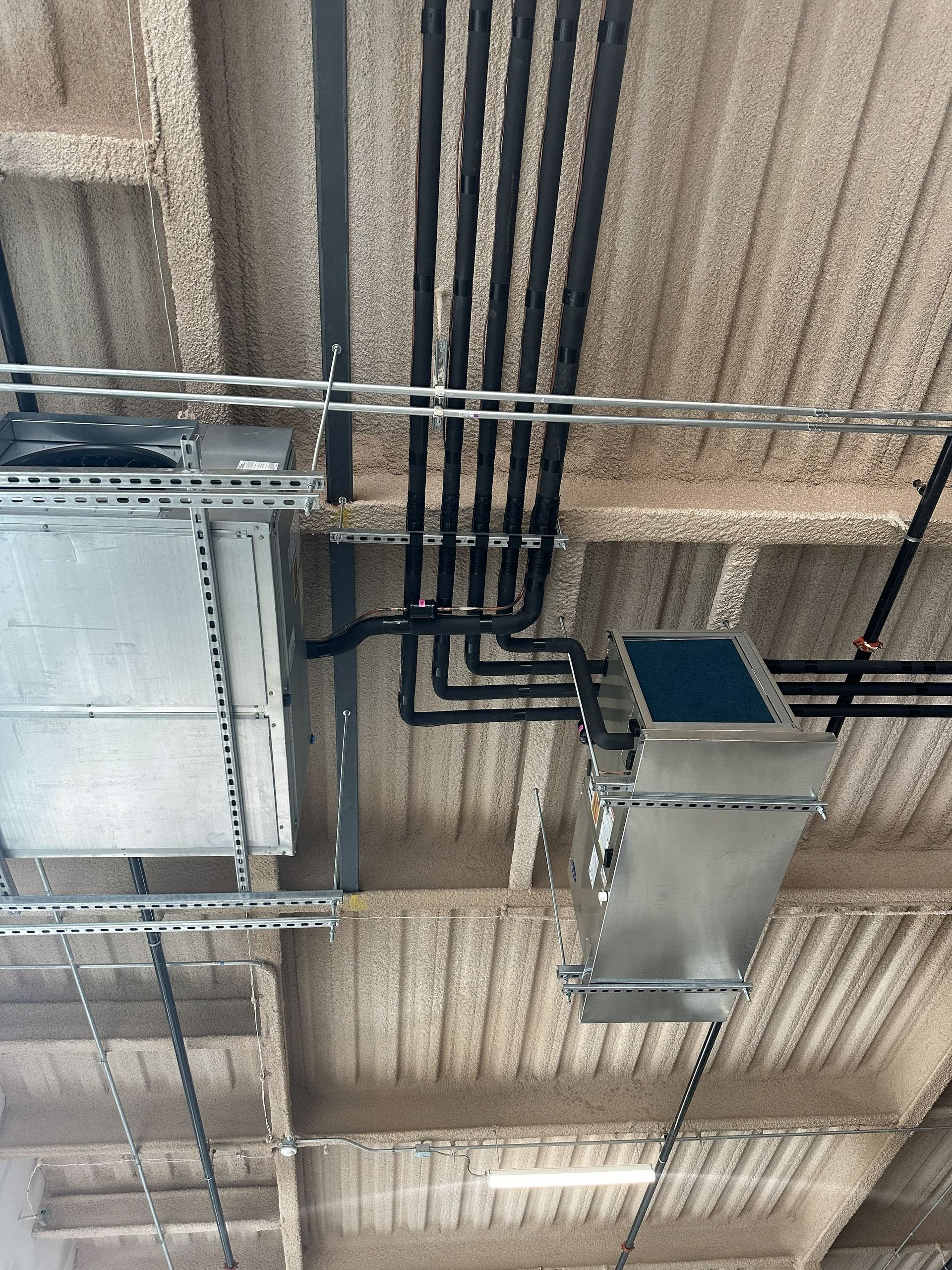 HVAC system components mounted on a concrete ceiling, including ducts, pipes, and electrical conduit.