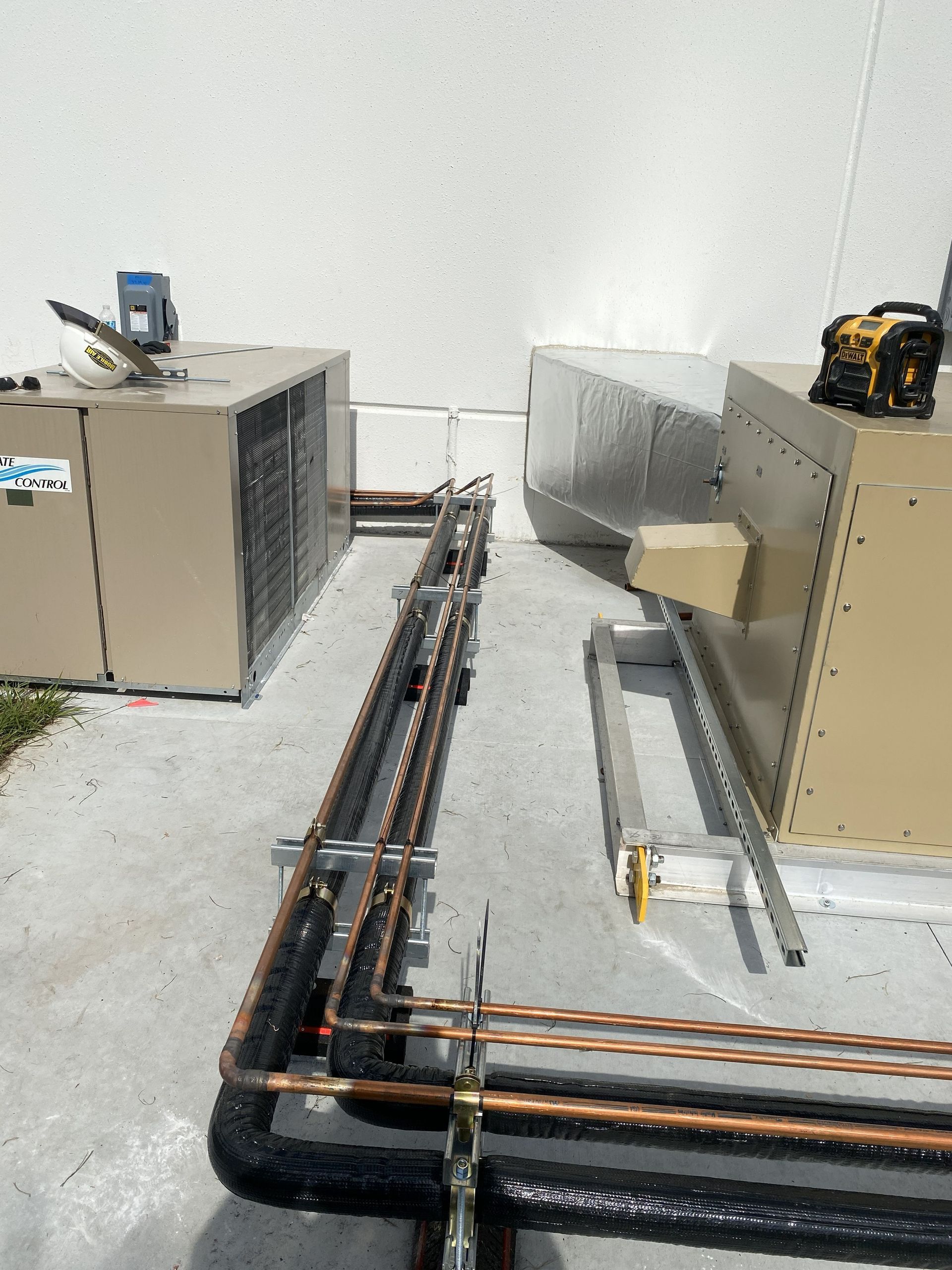 HVAC rooftop units with copper piping and tools on a flat surface against a white wall.