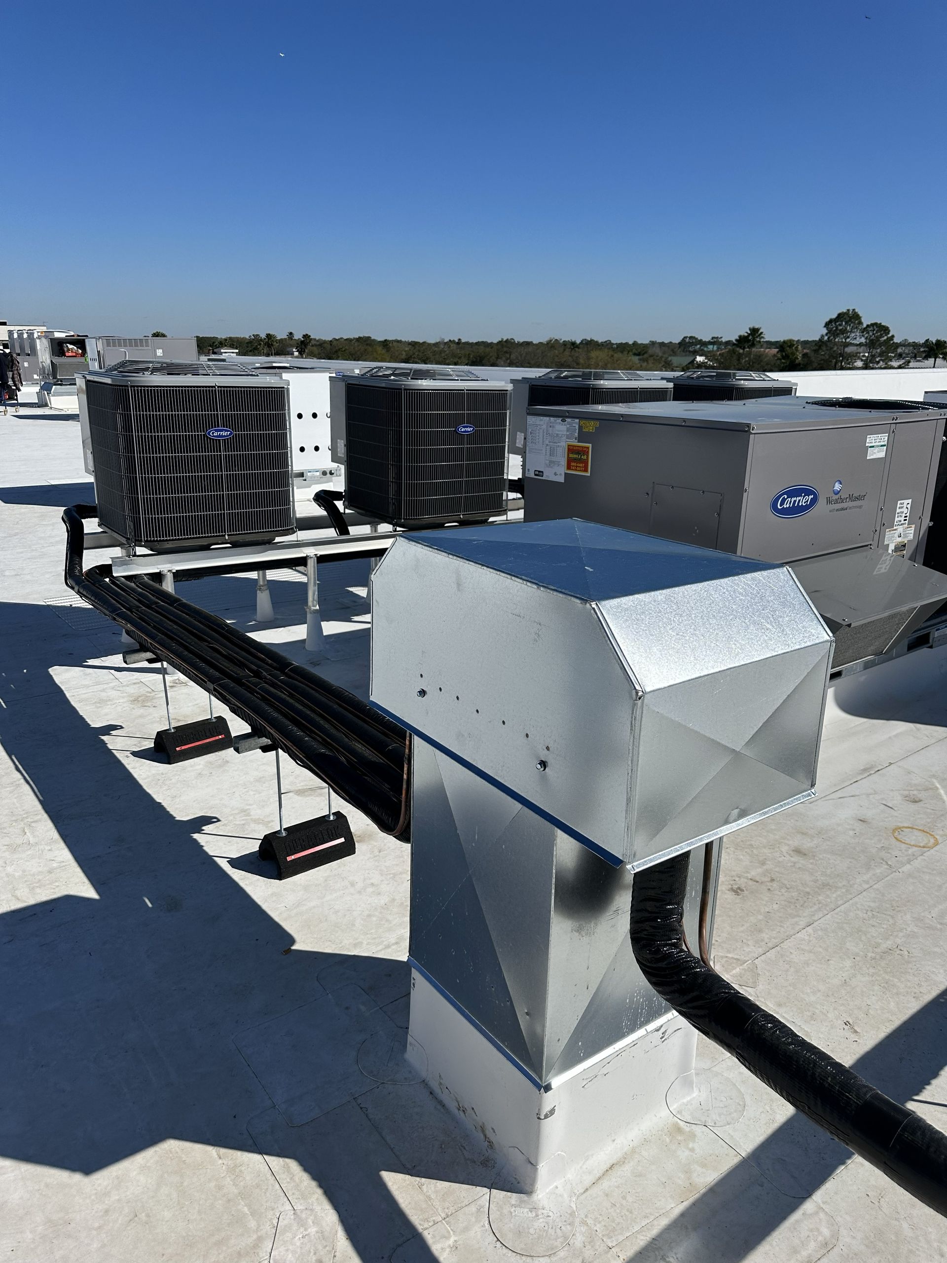 Rooftop HVAC units against a blue sky. Ductwork and silver metal vents are visible.