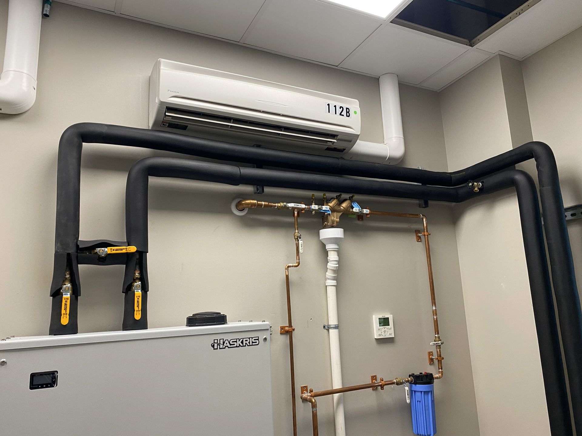 HVAC system with a wall-mounted unit and insulated black pipes connected to a boiler, with copper pipes and a filter.