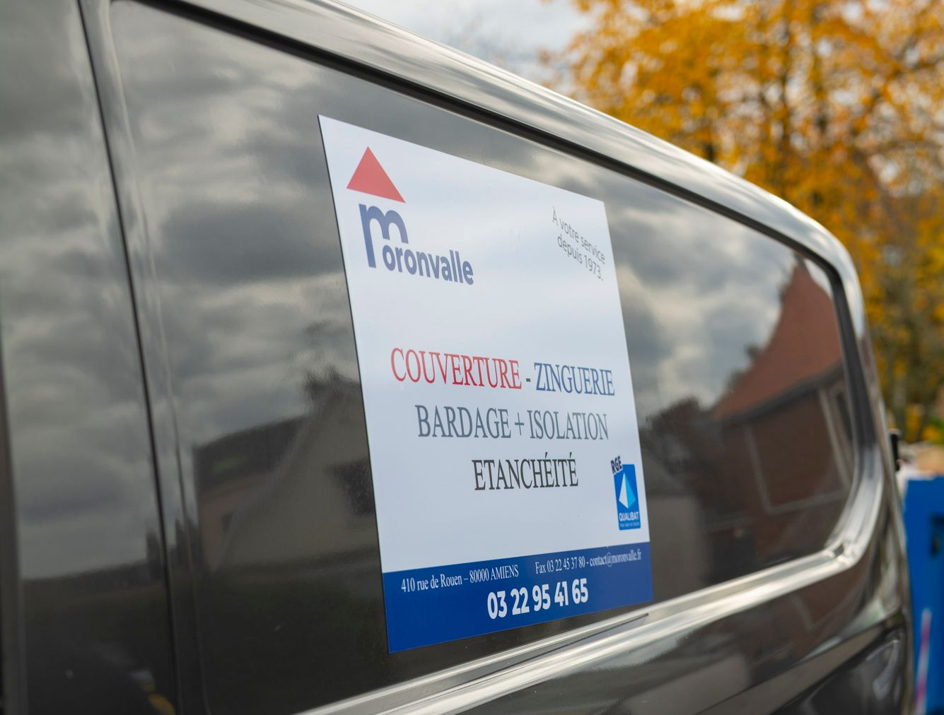 Fourgonnette gris foncé avec un panneau d'entreprise sur le côté ; le panneau comporte le logo et les coordonnées de l'entreprise.