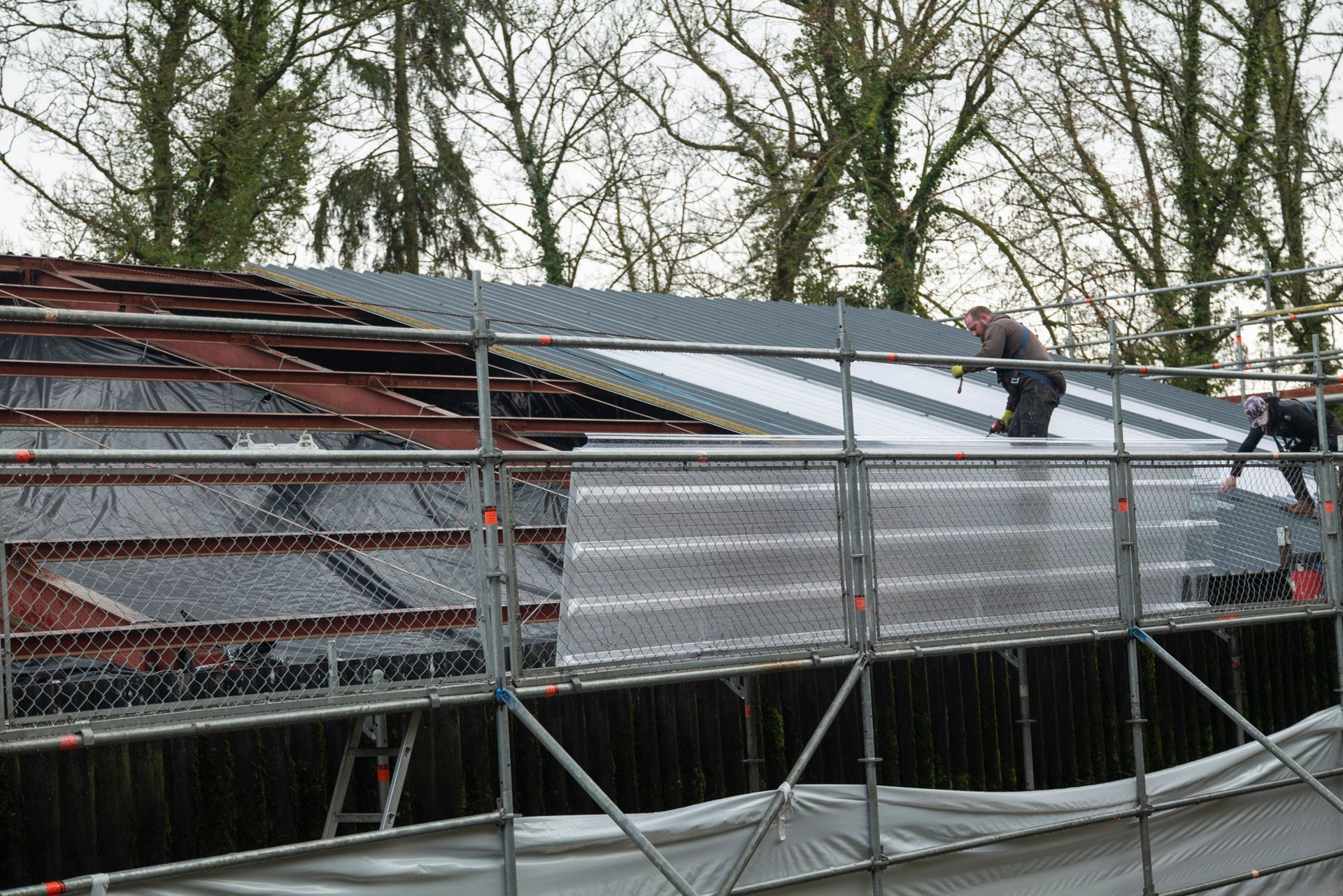 Toit en ardoise grise percé de deux puits de lumière reflétant un ciel bleu et le bâtiment adjacent.