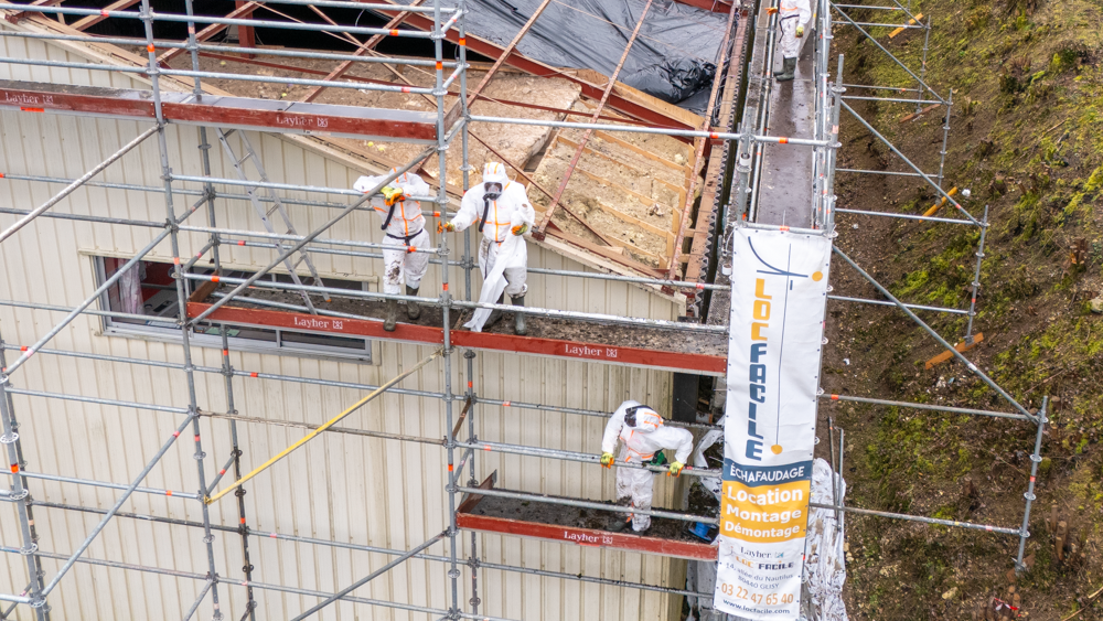 Un ascenseur orange est déployé vers un mur en tôle ondulée grise.