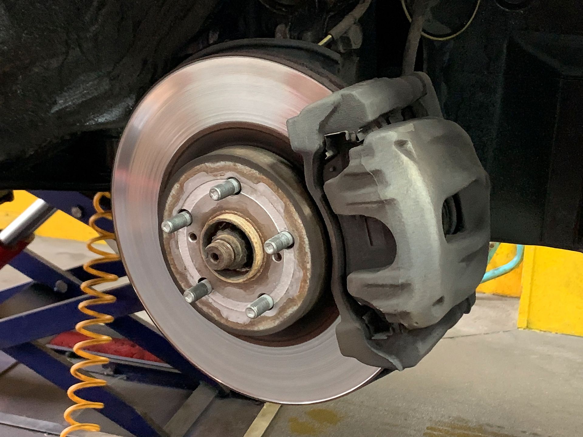 Close-up view of the disk brake of a car raised on a lift in a car repair shop.