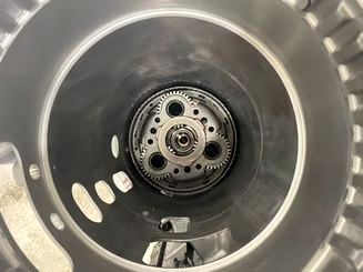 Inside view of a cylindrical metal object, revealing a gear assembly at the center. Gray and black color scheme, with details visible.