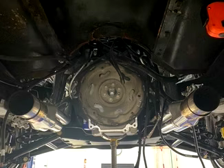 Undercarriage of a car with a visible engine, exhaust pipes, and wiring; viewed from below.
