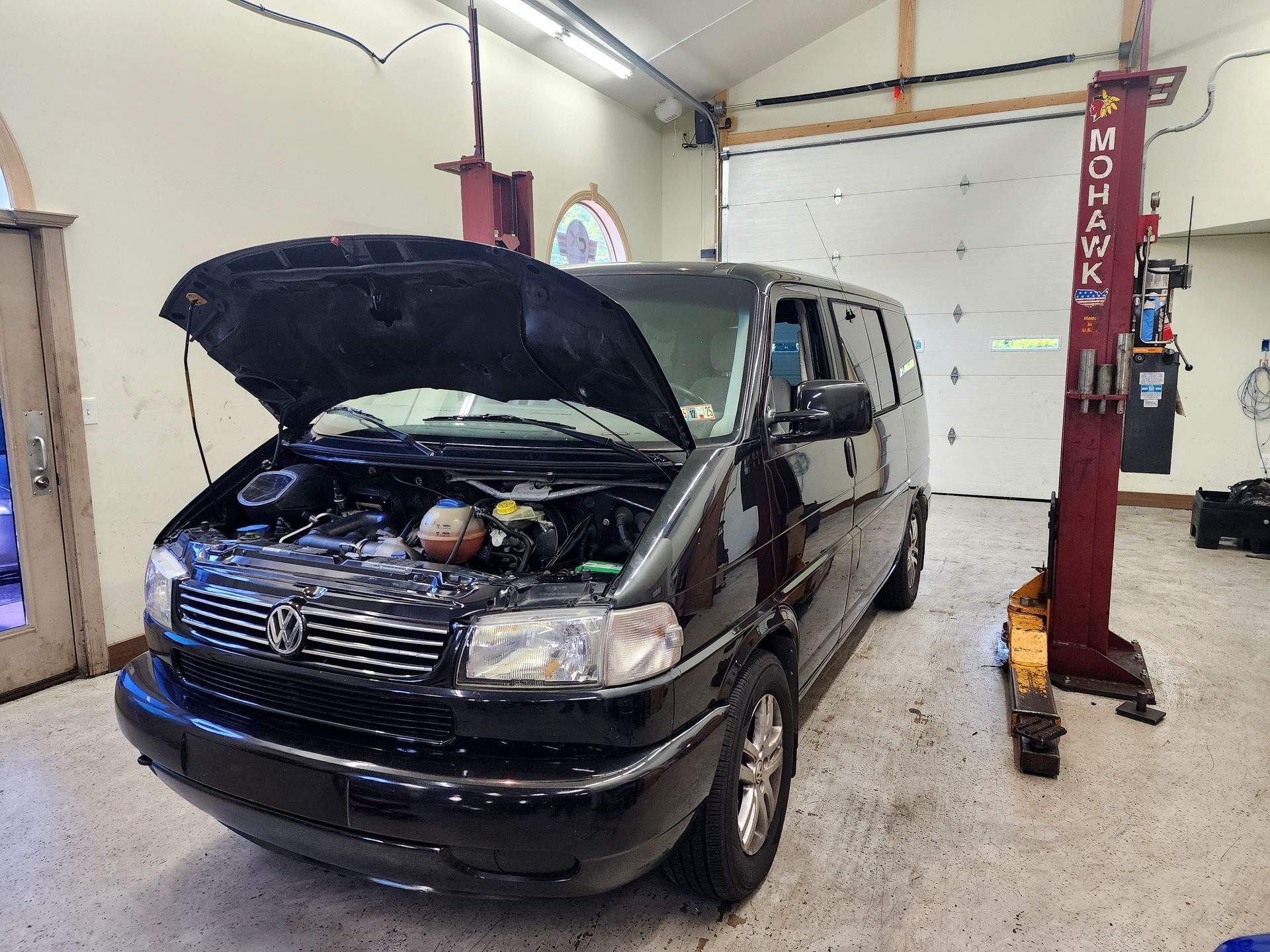 Black Volkswagen van with open hood in a garage, next to a car lift.