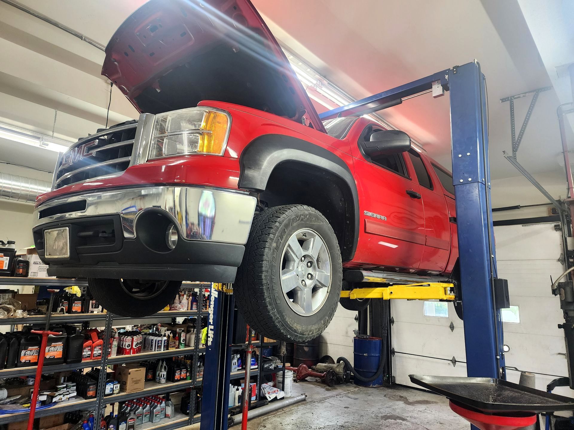 A red pickup truck is raised on a hydraulic lift in a garage. The hood is open, and the setting is a repair shop.