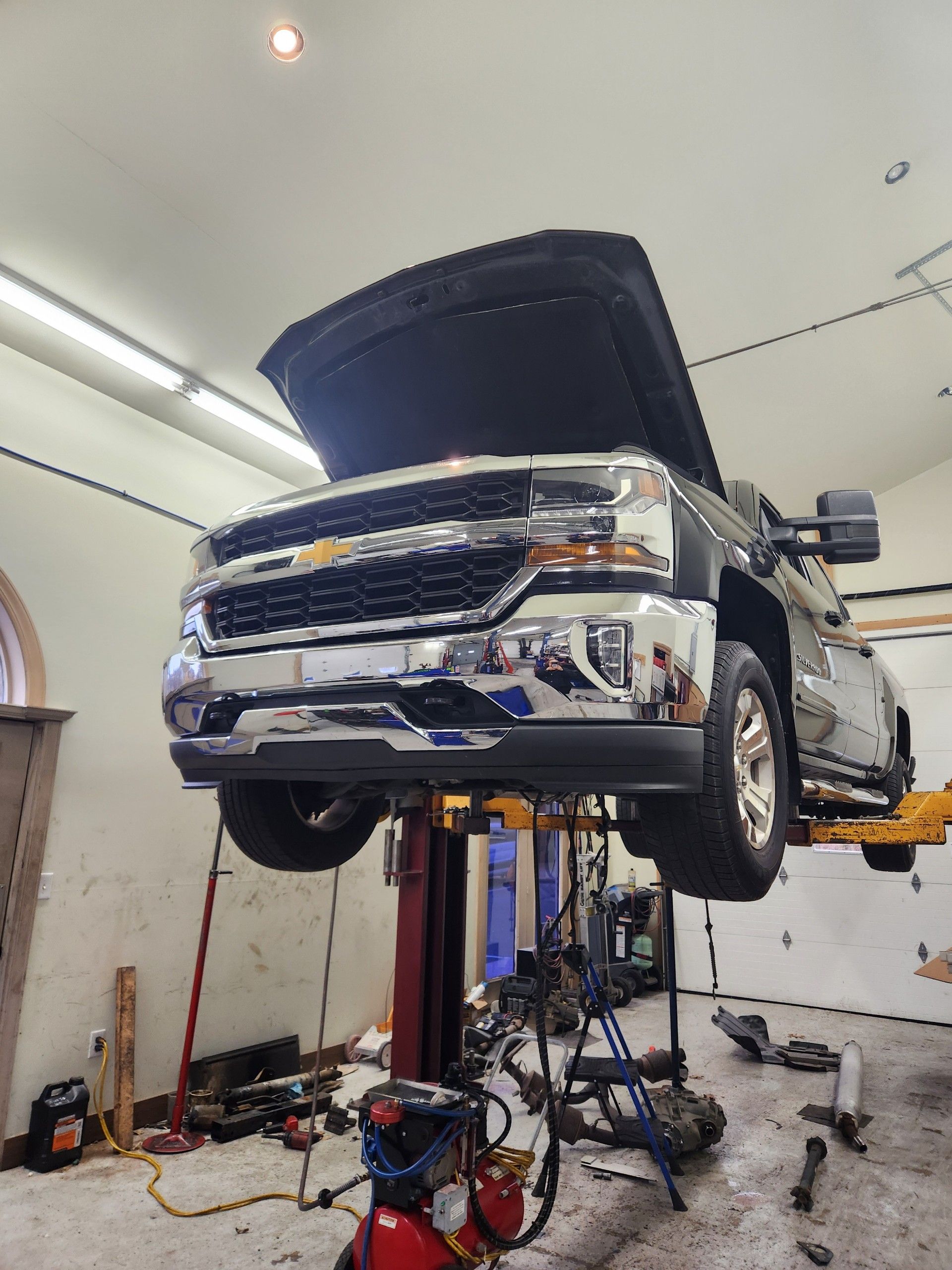 A black Chevrolet pickup truck raised on a lift in a garage with its hood open.