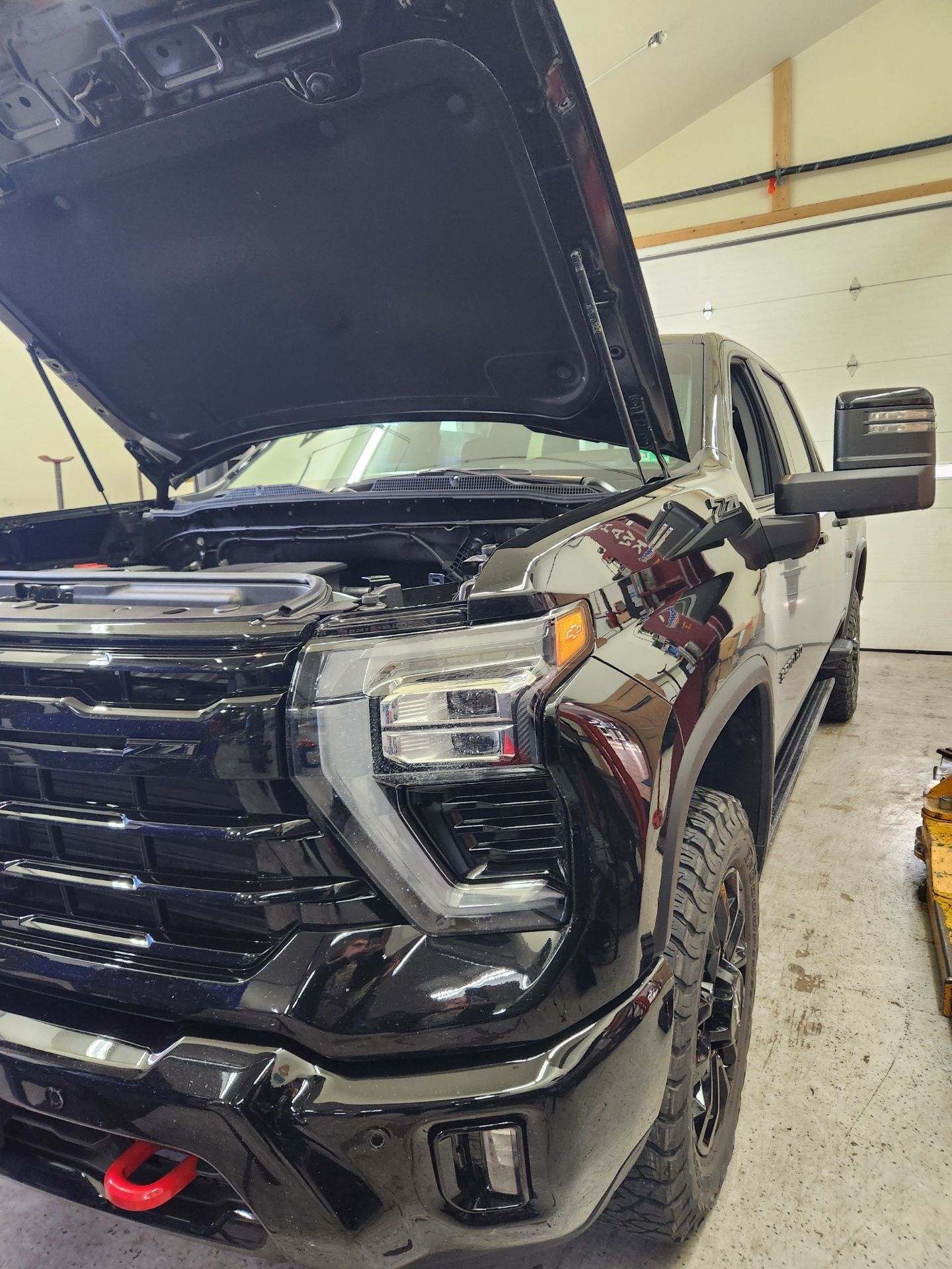 Black pickup truck with hood up, in a garage.