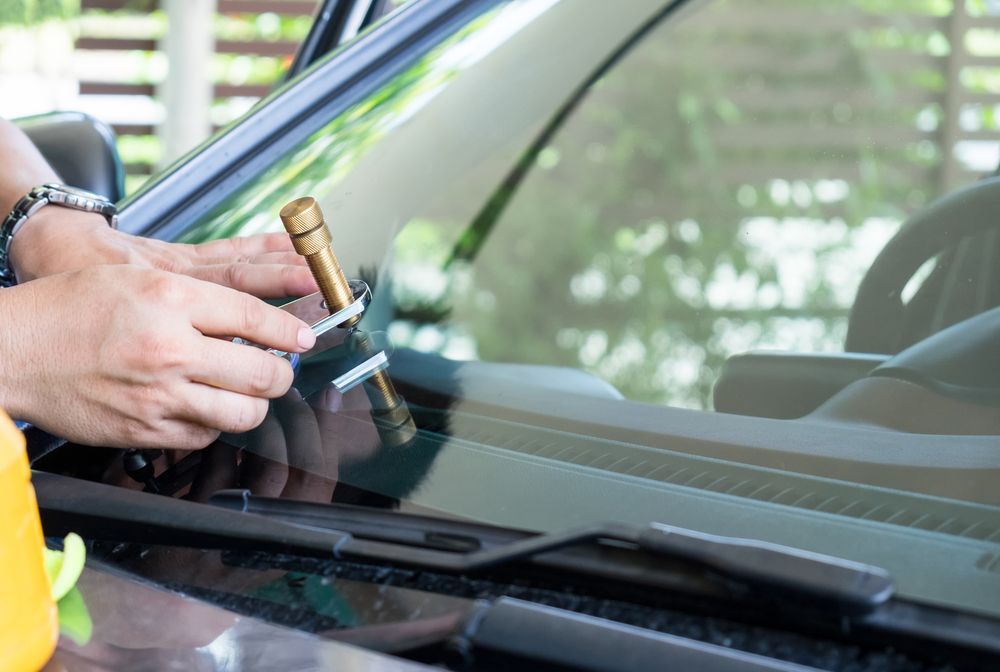 A Person Is Fixing A Windshield On A Car With A Screwdriver — Raymond Terrace Windscreen Services In Lake Macquarie, NSW