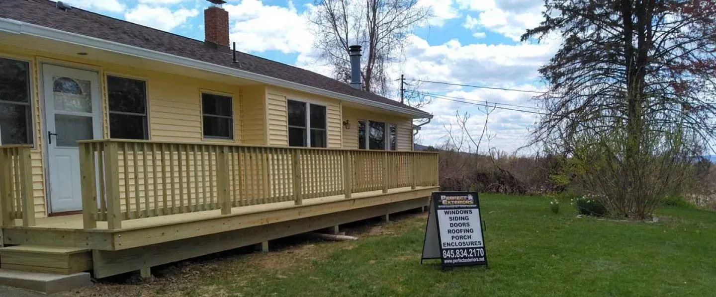 A house with a large deck and a for sale sign in front of it.
