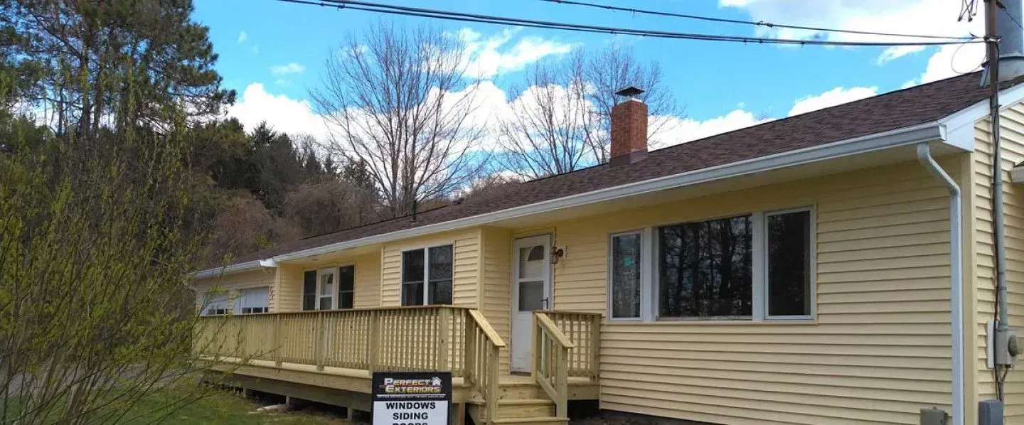 A yellow house with a wooden deck and a for sale sign in front of it.