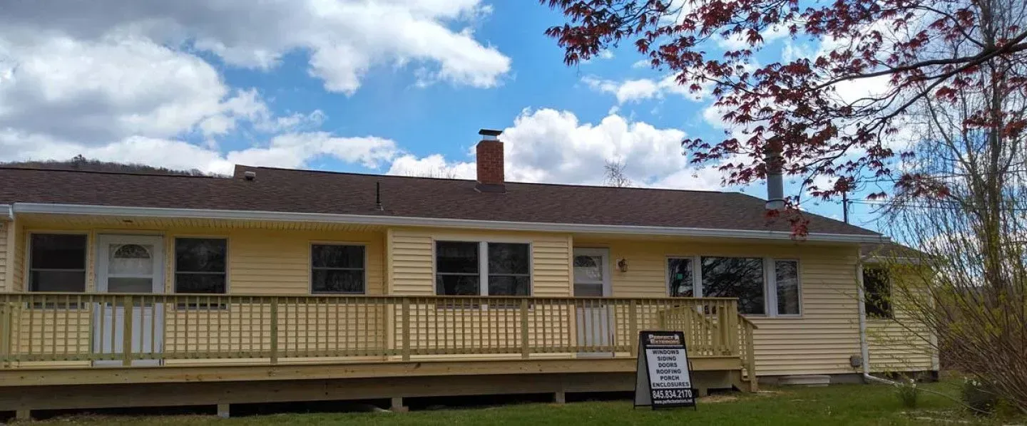 A yellow house with a wooden deck and a sign in front of it.