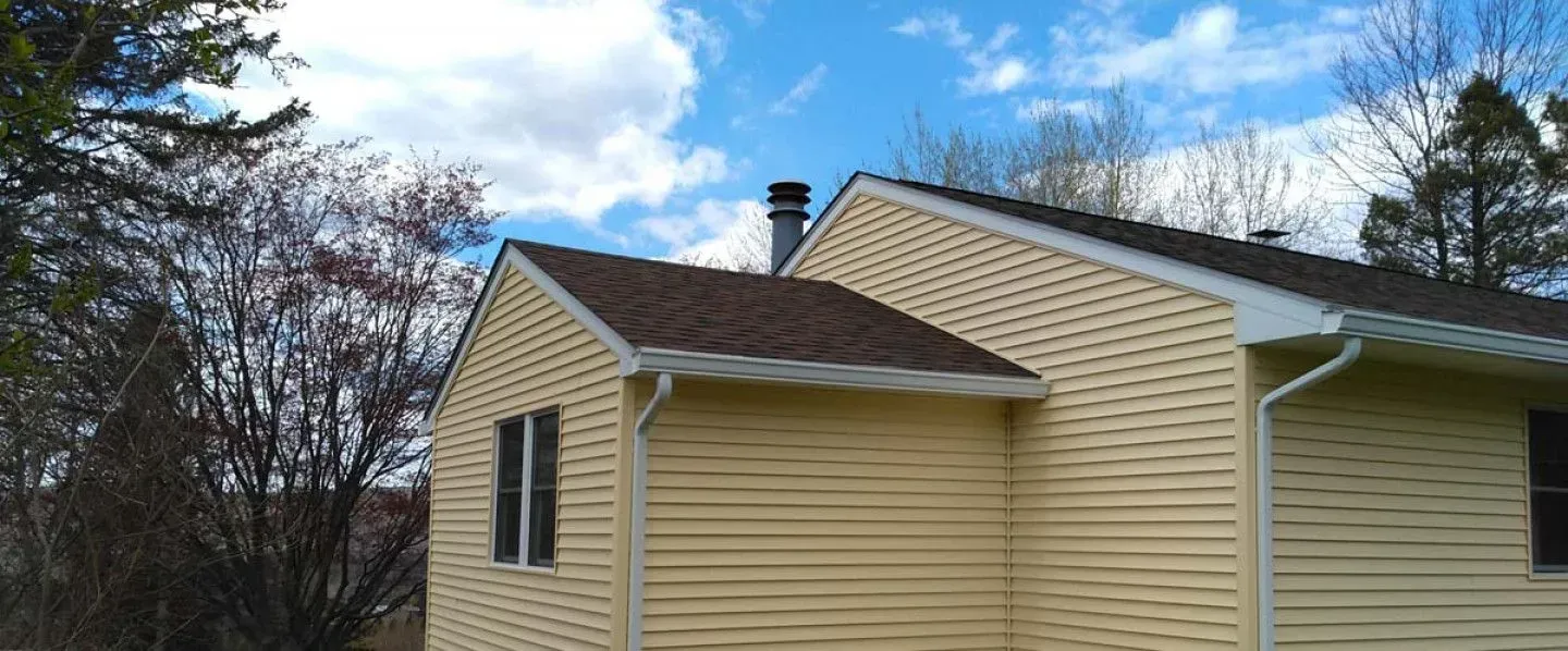 A yellow house with a brown roof and a chimney on top of it.