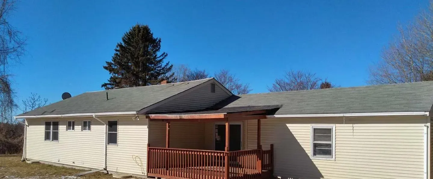 A white house with a gray roof and a porch on a sunny day.
