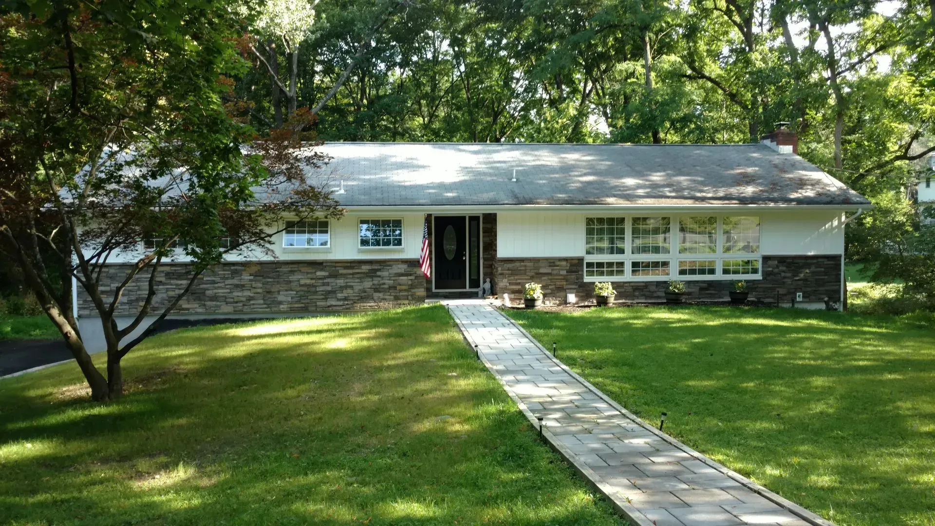 A house with a walkway leading to it is surrounded by trees and grass.