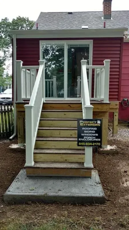 A red house with a wooden deck and stairs leading up to it.