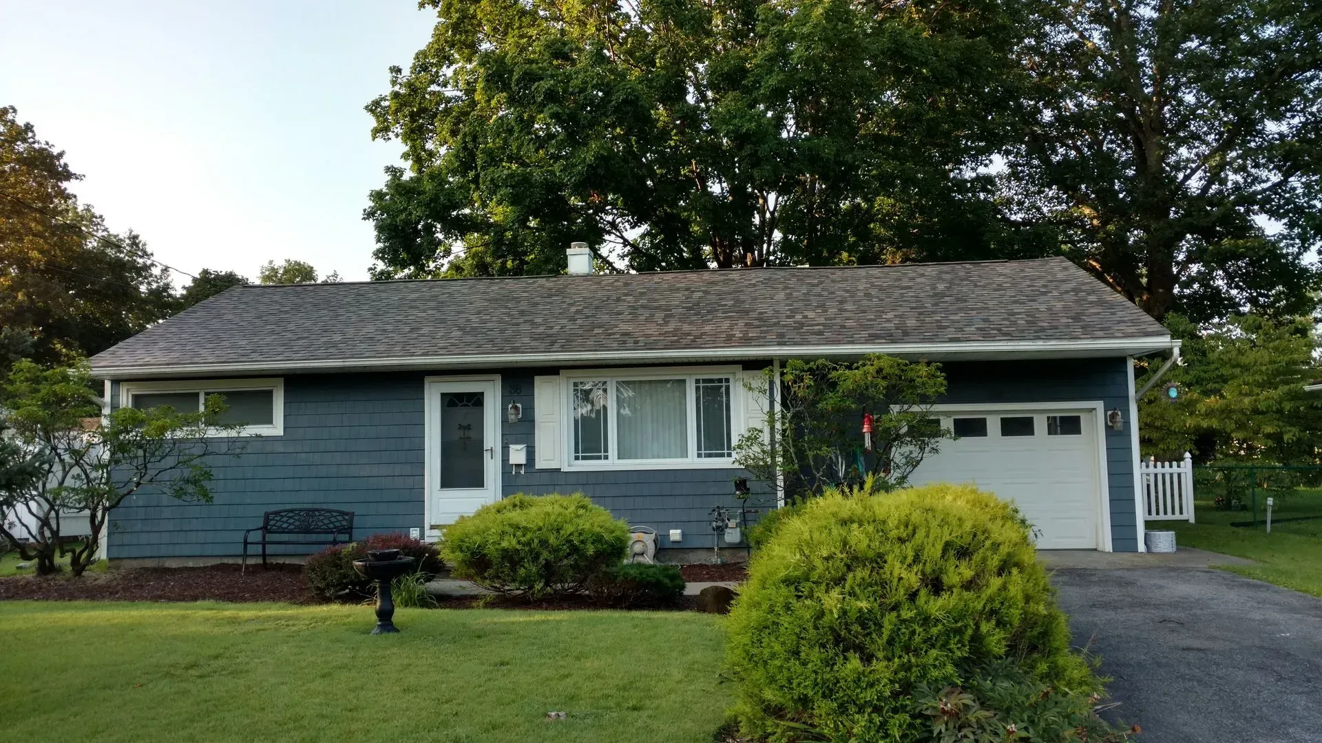 A blue house with a white garage door is surrounded by trees.