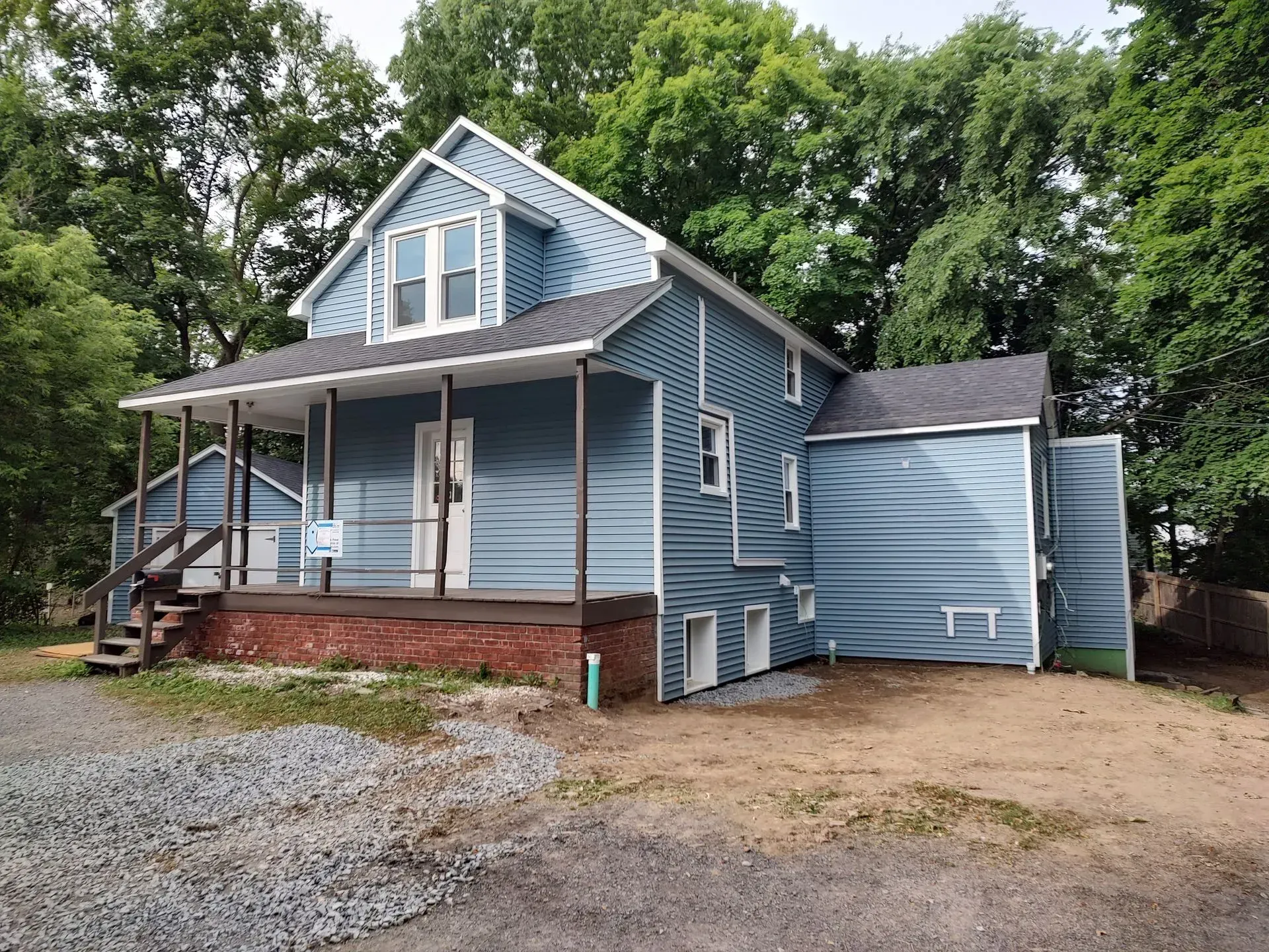 A blue house with a porch and a garage is surrounded by trees.