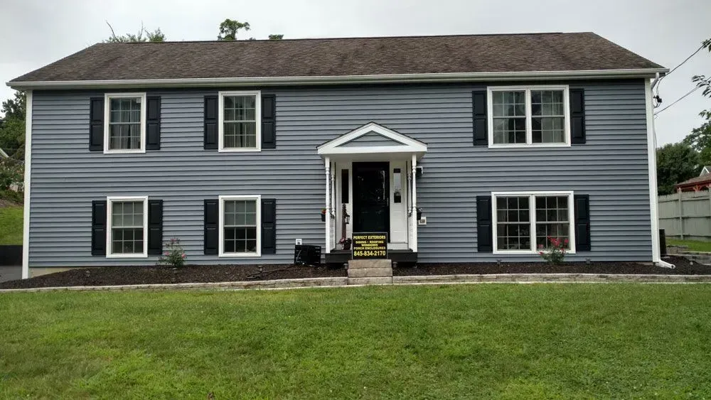 A large gray house with black shutters is sitting on top of a lush green lawn.