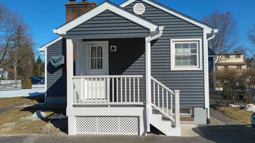 A small house with a porch and stairs on a sunny day.