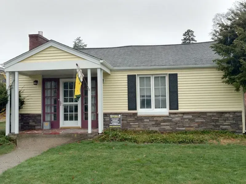 A yellow house with black shutters and a yellow flag on the porch.