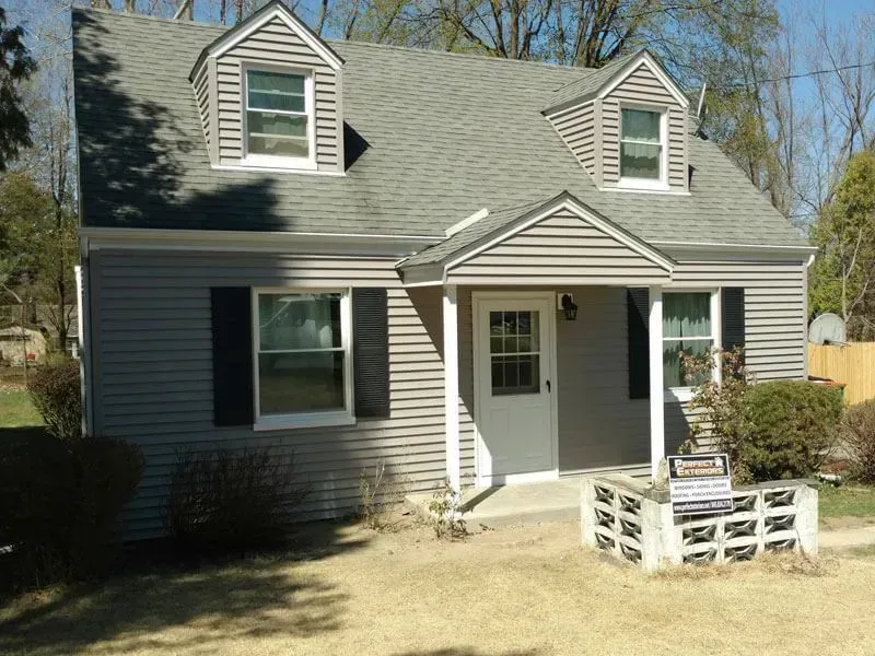 A small house with a gray siding and black shutters