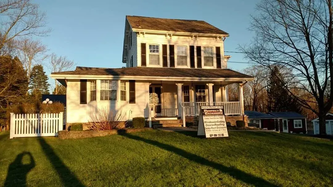 A large white house with a large porch is sitting on top of a lush green field.