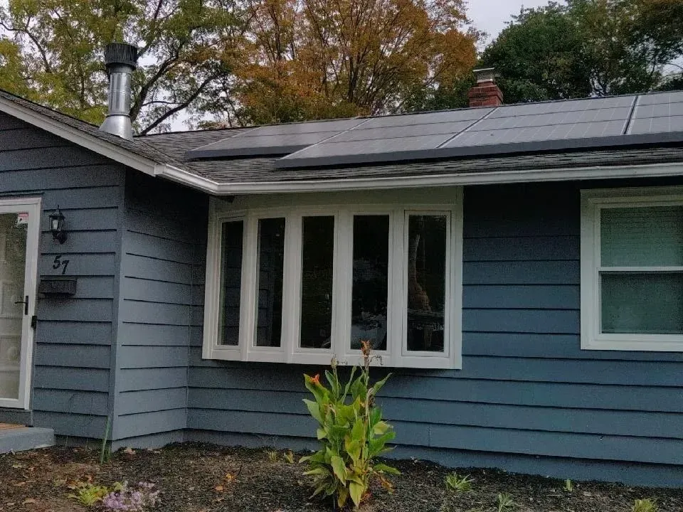 A blue house with white windows and solar panels on the roof.
