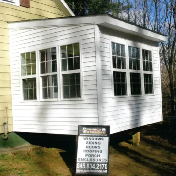A white building with a sign that says windows doors roofing porch enclosures